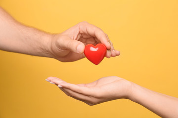 Man giving red heart to woman on yellow background, closeup. Donation concept
