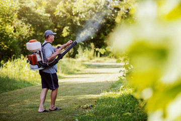 Side view of Caucasian mature peasant in working clothes, hat and with modern pesticide spray...
