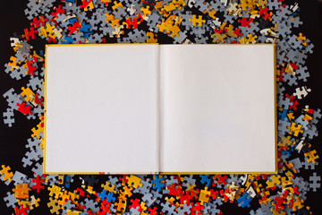 Blank book on a black background with puzzle pieces.