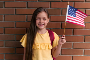 cute little girl smiling and holding American flag standing standing against brick wall