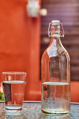 botella de agua con vaso sobre mesa y fondo rojo y marrón