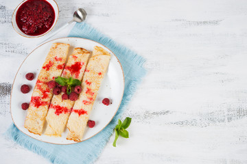 Thin pancakes for Breakfast on a plate with raspberry jam on a light background
