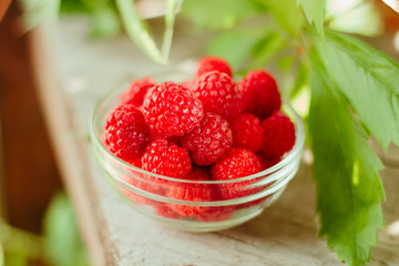 glass bowl full of raspberries on wooden garden table  background