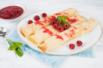 Thin pancakes for Breakfast on a plate with raspberry jam on a light background