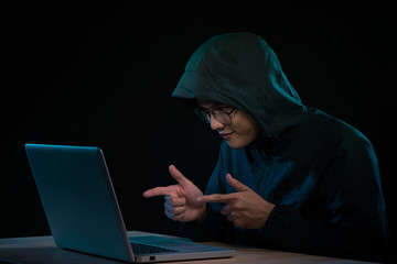 Successful male hacker poses in front of laptop computer, clenches fists, dressed in black clothes, rejoices finishing bad data virus,