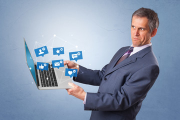 Man holding laptop with different types of social media symbols and icons