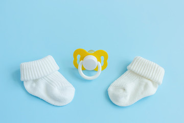 Baby accessories for newborns: socks and soother on blue background. Motherhood concept. Top view, flat lay composition. Copy space for text.