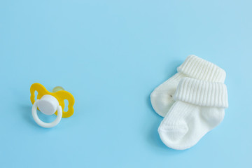 Baby accessories for newborns: socks and soother on blue background. Motherhood concept. Top view, flat lay composition. Copy space for text.