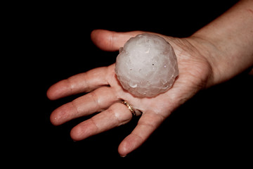 Golf ball size hailstone held in palm of hand with black background.