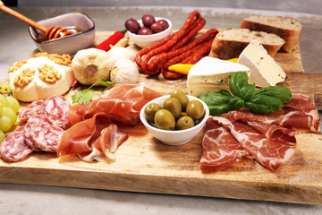 Cutting board with prosciutto, salami, cheese,bread and olives on dark stone background