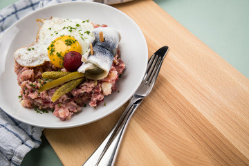 Norddeutscher Hamburger Labskaus mit Rindfleisch Corned Beef, Rote Beete, Kartoffeln, Saure Gurken, Spiegelei und Rollmops auf Teller