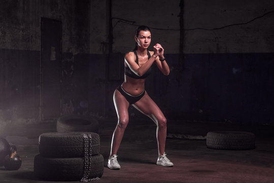 Squatting muscular woman on the old garage background. fitness, sport, exercising and healthy lifestyle concept - woman doing squats outdoors.