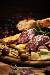 antipasto various appetizer. Cutting board with salami, cheese, bread and olives on dark wooden background