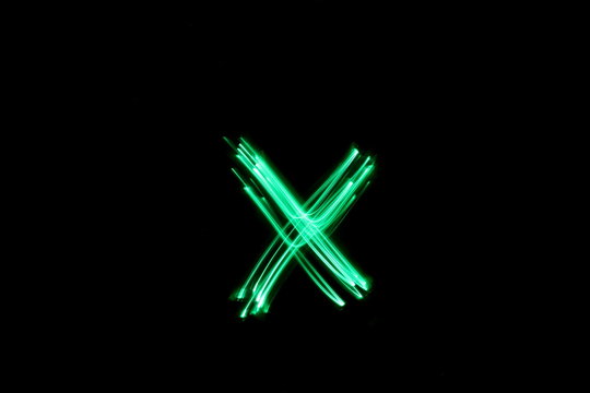 Long exposure photograph, light painting photography.  Letter x of an alphabet series, single letter, in neon green light, against a black background