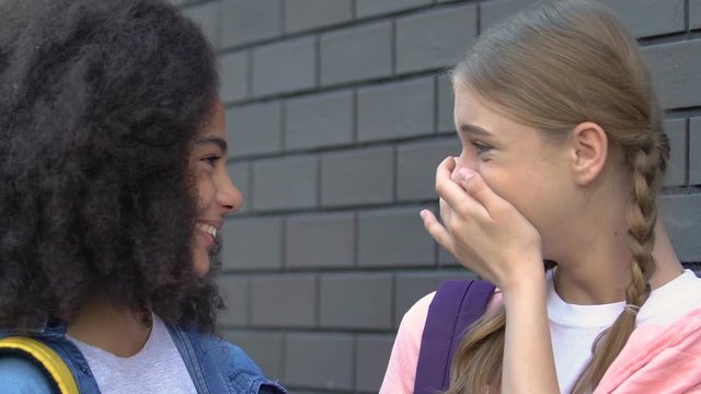 Female teenagers gossiping in schoolyard, spreading rumors about classmates