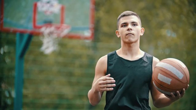A man standing on a sports ground and holding a basketball ball - moving the ball between his hands