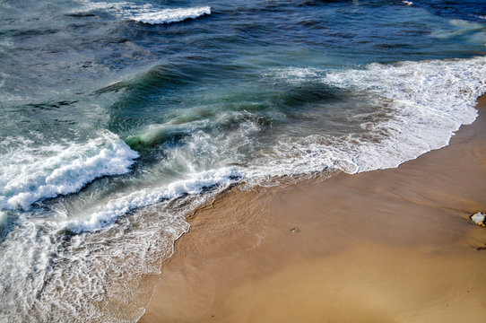 Dark blue waves with white foam on yellow sand. Sand background