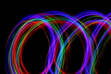 Long exposure photograph of neon multi colour in an abstract swirl parallel lines pattern against a black background. Light painting photography.