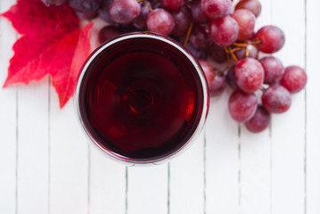 glass of red wine and grapes on white wooden table