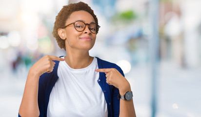 Young beautiful african american woman wearing glasses over isolated background looking confident with smile on face, pointing oneself with fingers proud and happy.