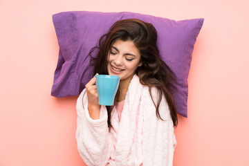 Happy teenager girl in dressing gown over pink backgrounnd and holding a cup of coffee