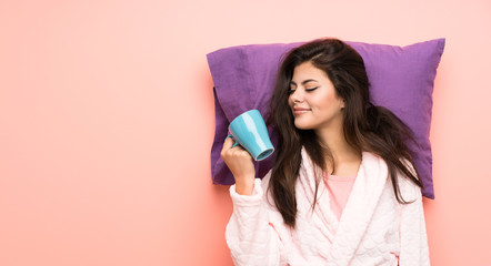 teenager girl in dressing gown over pink backgrounnd and holding a cup of coffee