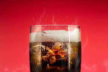 Soft drink glass with ice splash on cool smoke background. Cola glass with summer refreshment.