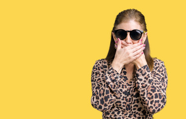 Fototapeta premium Middle age mature rich woman wearing sunglasses and leopard dress over isolated background shocked covering mouth with hands for mistake. Secret concept.