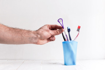 Hand put a tongue brush into a cup with toothbrushes
