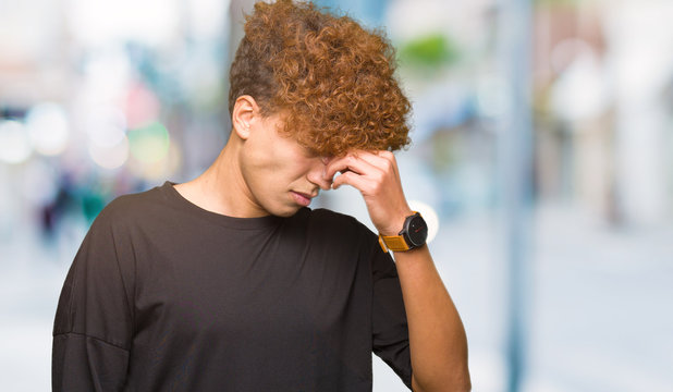 Young handsome man with afro hair wearing black t-shirt tired rubbing nose and eyes feeling fatigue and headache. Stress and frustration concept.