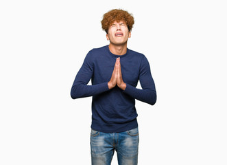 Young handsome man with afro hair begging and praying with hands together with hope expression on...