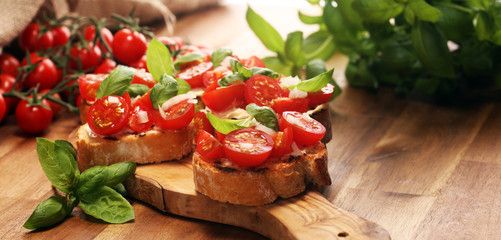 Traditional italian antipasto bruschetta appetizer with cherry tomatoes, cream cheese, basil leaves and balsamic vinegar on cutting board. Antipasti