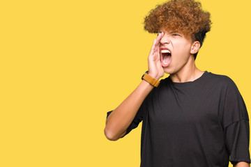 Young handsome man with afro hair wearing black t-shirt shouting and screaming loud to side with hand on mouth. Communication concept.