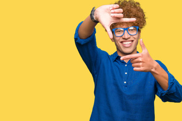 Young handsome man with afro hair wearing blue glasses smiling making frame with hands and fingers with happy face. Creativity and photography concept.