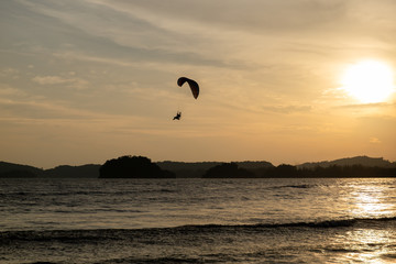 beautiful Silhouette of paraglider flying in the sky of sunset on the beach.