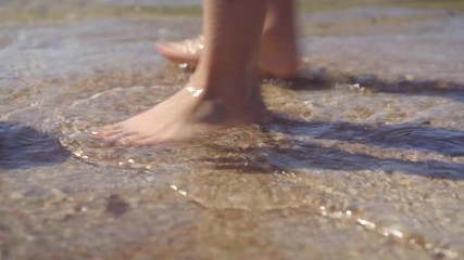 Child feet barefoot walk along a shore.  Picks up a black float thrown by surf