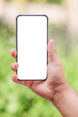 Hand holding empty white cellphone on abstract blurry green outdoor background. Device mockup concept/cellphone Green bokeh background