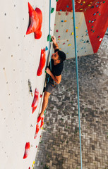 Sportive man climbs up on artificial rock wall