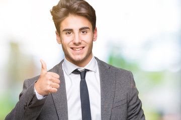 Young business man wearing suit and tie over isolated background doing happy thumbs up gesture with hand. Approving expression looking at the camera with showing success.