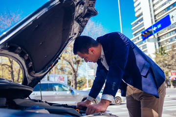A handsome businessman wearing blue blazer lifting up the hood of his car and checking the oil...