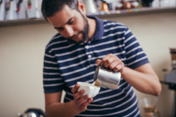 Young man pouring milk into a cup of coffee