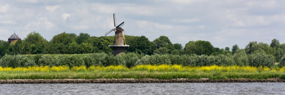 View on the shore of the Merwede River in the Netherlands, Typical Dutch landscape with traditional windmill to provide energy and power. Real Dutch weather with wind, clouds and sun.
