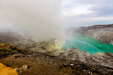 Crater of a volcano with a green sulfuric volcanic lake and volcanic smoke. View of the smoking volcano Kawah Ijen in Indonesia. Mountain landscape
