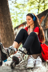 Happy joyful young woman wearing roller skates sitting in park
