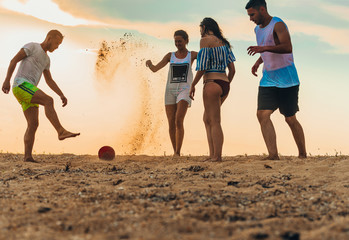 Four people playing soccer or football on sandy beach on summer holiday