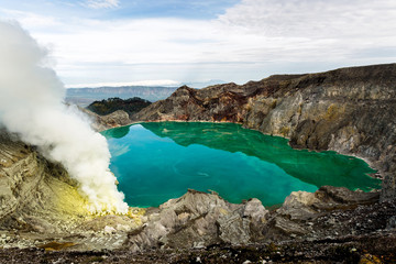 Crater of a volcano with a green sulfuric volcanic lake and volcanic smoke. View of the smoking volcano Kawah Ijen in Indonesia. Mountain landscape