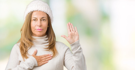 Beautiful middle age woman wearing winter sweater and hat over isolated background Swearing with...