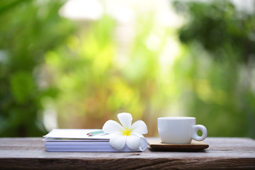 White coffee cup and notebooks flower on brown wooden table at outdoor