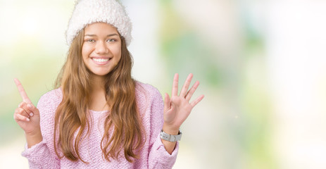 Young beautiful brunette woman wearing sweater and winter hat over isolated background showing and pointing up with fingers number six while smiling confident and happy.