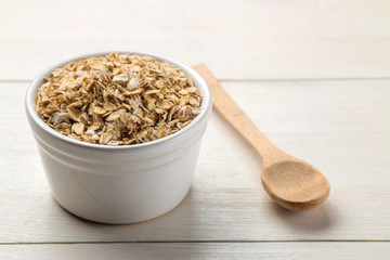 Dry oatmeal flakes in a bowl and spoon on a white wooden table. healthy nutrition. healthy food.
